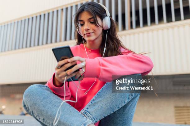 beautiful teenage girl wearing headphones while using smart phone - alleen één tienermeisje stockfoto's en -beelden