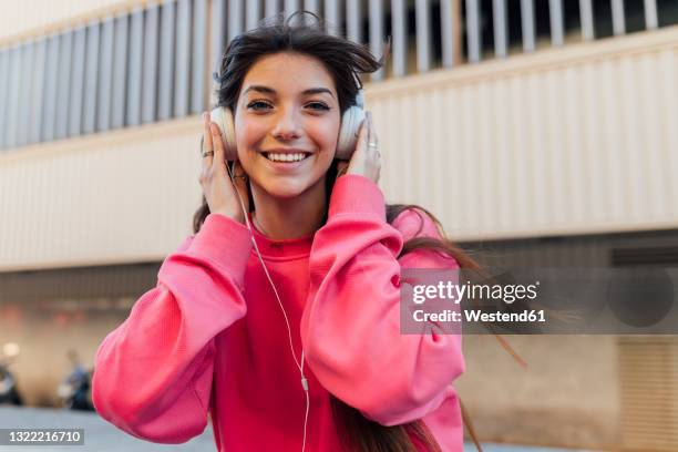 smiling teenage girl holding headphones while listening music - magenta stockfoto's en -beelden