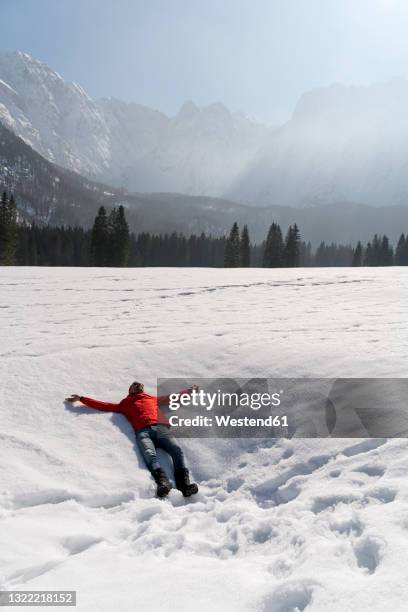 carefree man with arms outstretched lying on snow in winter - friuli foto e immagini stock