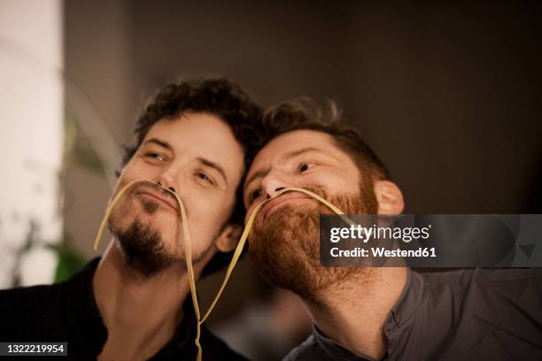 playful men playing with ribbon pasta at home - bromance stock-fotos und bilder