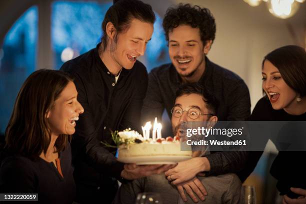 surprised man looking at birthday cake amidst male and female friends at home - 40 birthday stock pictures, royalty-free photos & images