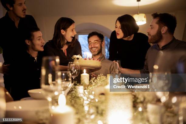 male and female friends cheering during birthday celebration of smiling man at home - 40 birthday foto e immagini stock