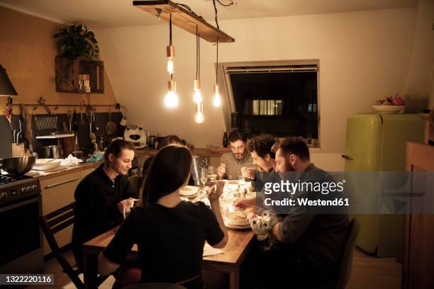 male and female friends eating pasta at dining table in kitchen - warmes abendessen stock-fotos und bilder