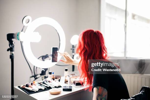 female artist with dyed red hair using smart phone while vlogging at studio - influencers stock pictures, royalty-free photos & images