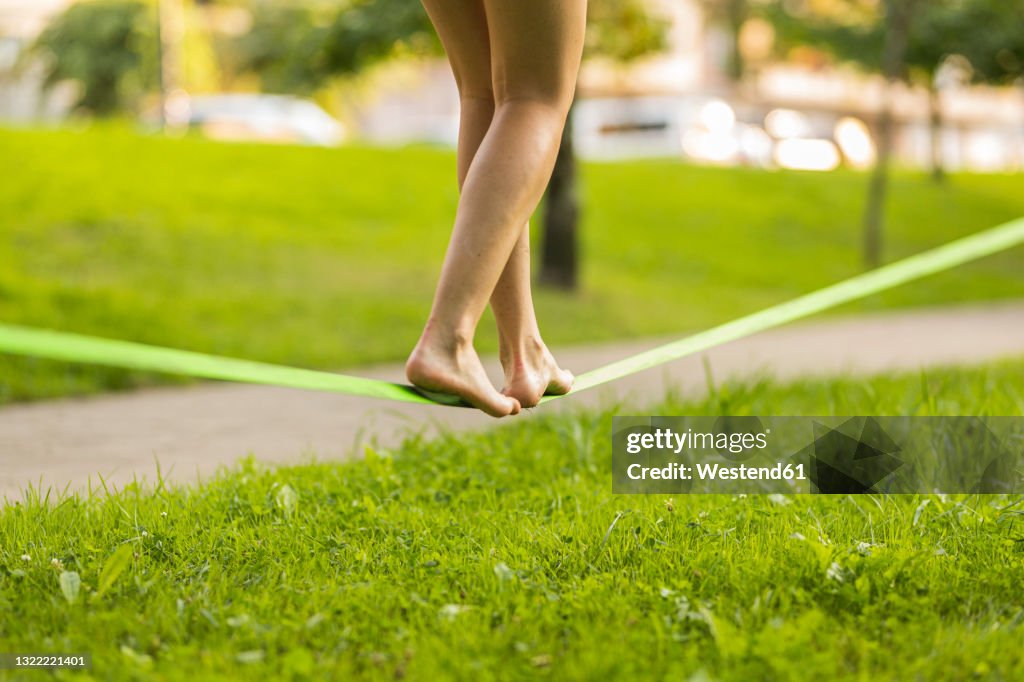 Young woman balancing barefoot on slackline in public park