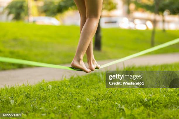 young woman balancing barefoot on slackline in public park - slacklining stock pictures, royalty-free photos & images