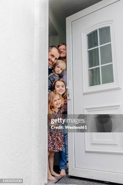 smiling family peeking through door at entrance of house - peer foto e immagini stock