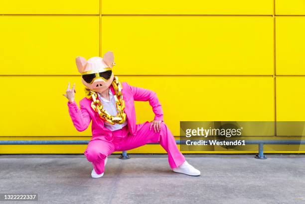 woman wearing vibrant pink suit, pig mask and large golden chain crouching in front of yellow wall - millionnaire stock pictures, royalty-free photos & images