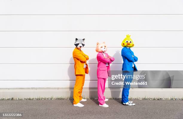 three people wearing vibrant suits and animal masks posing side by side in front of white wall - by racoon on white photos et images de collection