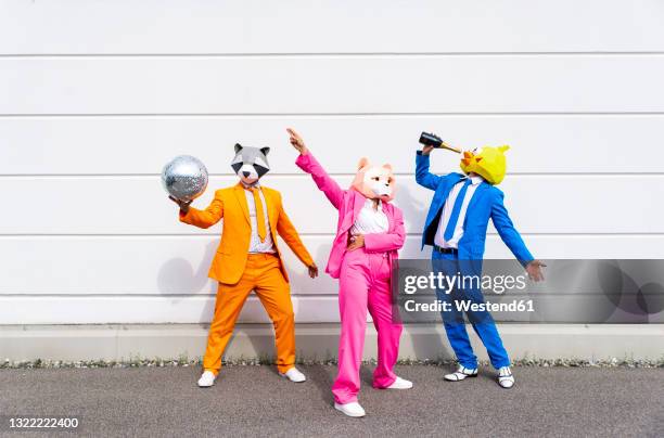 three people wearing vibrant suits and animal masks partying in front of white wall - funny dressed man stock-fotos und bilder