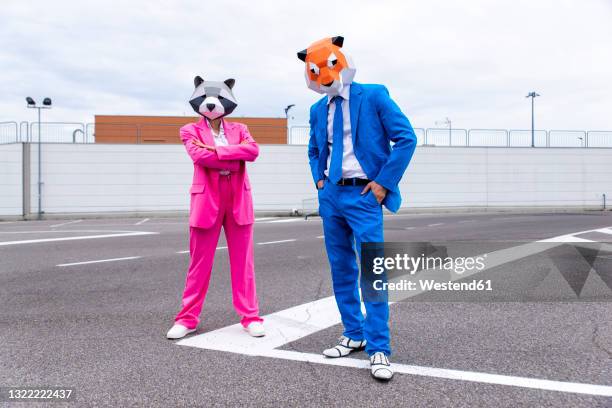 man and woman wearing vibrant suits and animal masks posing side by side in empty parking lot - pink suit stockfoto's en -beelden