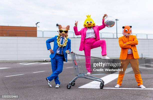 funny characters wearing animal masks and colored business suits having fun on empty parking lot - showing off foto e immagini stock