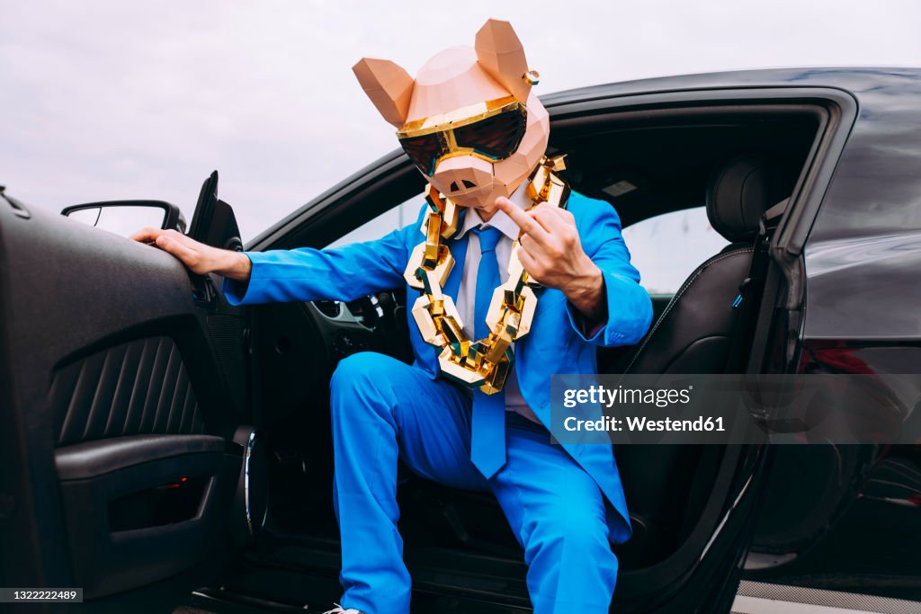 Funny character wearing animal mask and blue business suit showing middle finger from car