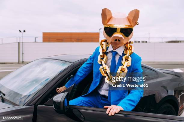 funny character wearing animal mask and blue business suit getting in car - reichtum stock-fotos und bilder