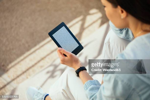 woman reading an e-book while sitting on steps - e reader stock pictures, royalty-free photos & images
