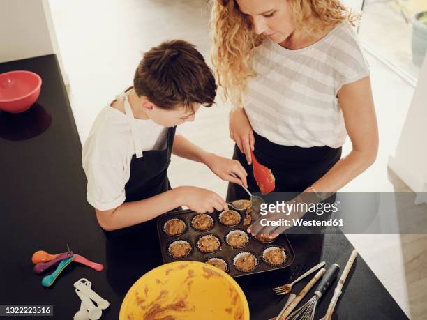 mother teaching son to fill muffin tray with batter in kitchen - baking dish stock pictures, royalty-free photos & images