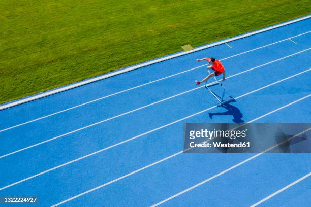 young man jumping over hurdle - hordelopen atletiekonderdeel stockfoto's en -beelden
