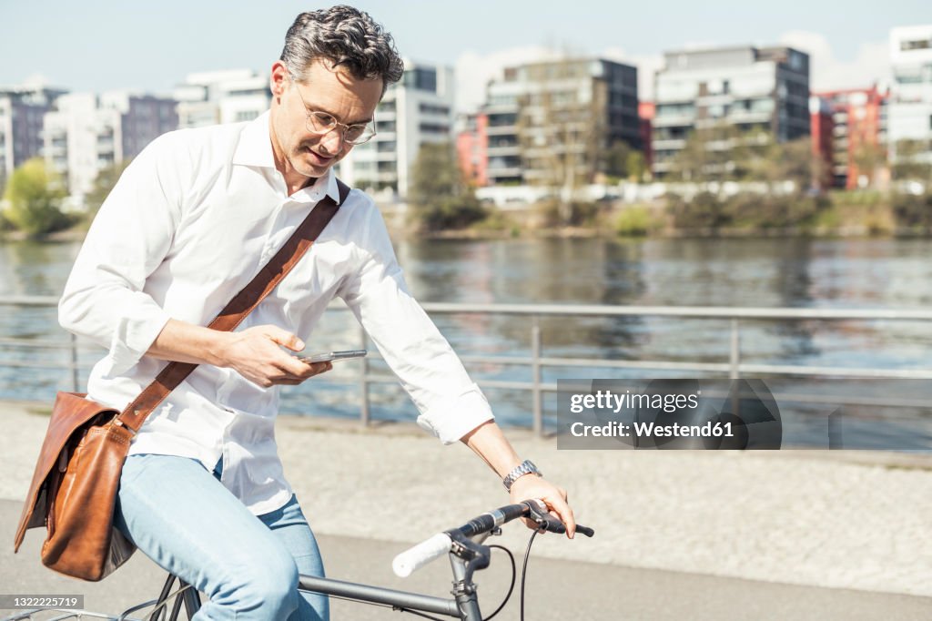 Businessman using mobile phone while cycling bicycle on sunny day