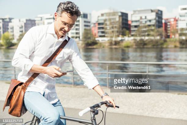 businessman using mobile phone while cycling bicycle on sunny day - hesse germany stock pictures, royalty-free photos & images