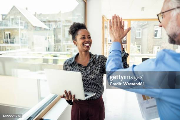 cheerful businesswoman with laptop doing high-five with male colleague in office - dammi un cinque foto e immagini stock