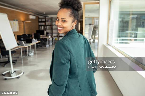 businesswoman smiling while looking over shoulder at office - looking over shoulder photos et images de collection