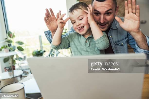 mischievous father and son teasing while sitting with laptop at home - protruding stock pictures, royalty-free photos & images