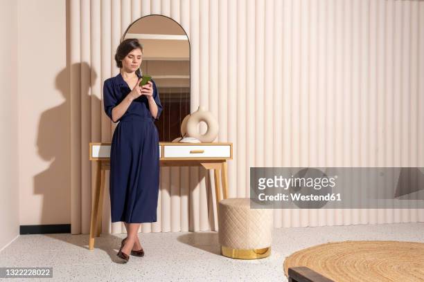 young woman using smart phone while leaning on table - full length mirror stock-fotos und bilder