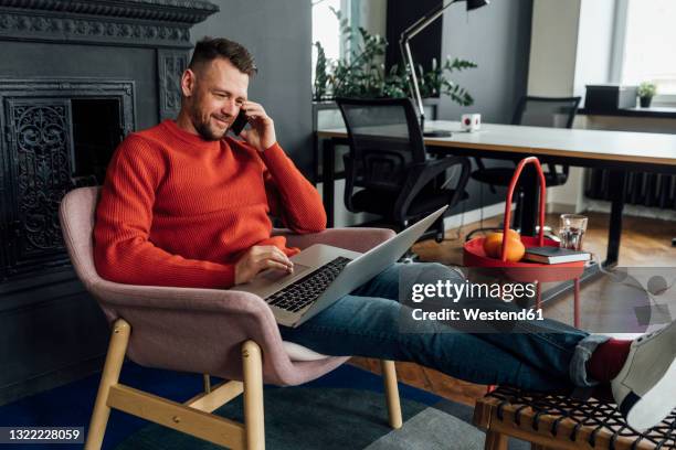 male entrepreneur using laptop while talking on mobile phone at office - red and white people stock pictures, royalty-free photos & images