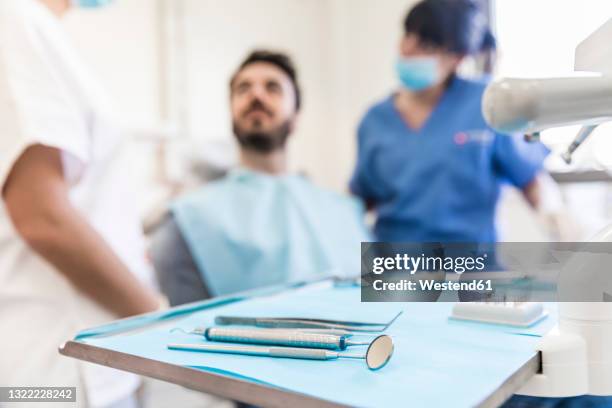 dental equipments on tray with female dentists and male patient in background at medical clinic - dentista foto e immagini stock