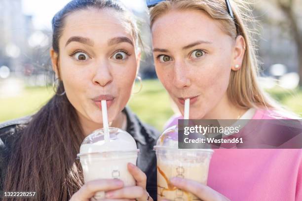 surprised female friends drinking milkshakes at park - milkshake stock pictures, royalty-free photos & images