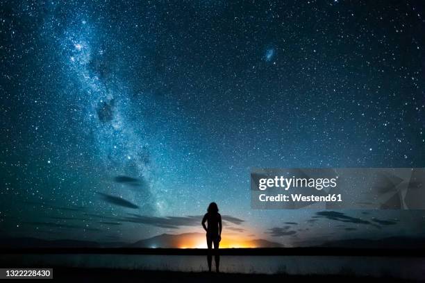 new zealand, canterbury, twizel, silhouette of man looking at lake poaka under starry sky - new zealand night stock pictures, royalty-free photos & images