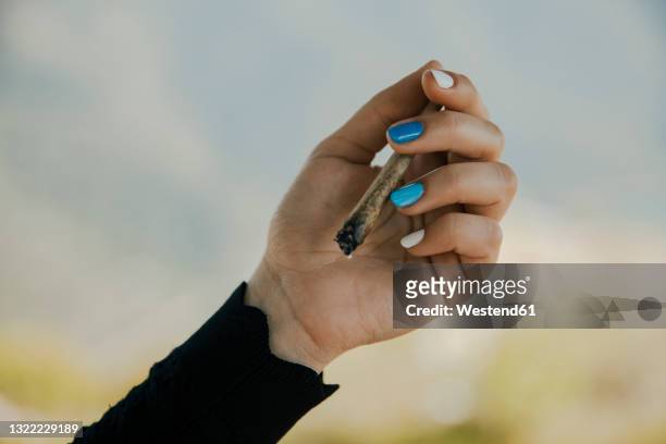 young woman holding burning marijuana cigarette in hand - joint body part stock-fotos und bilder