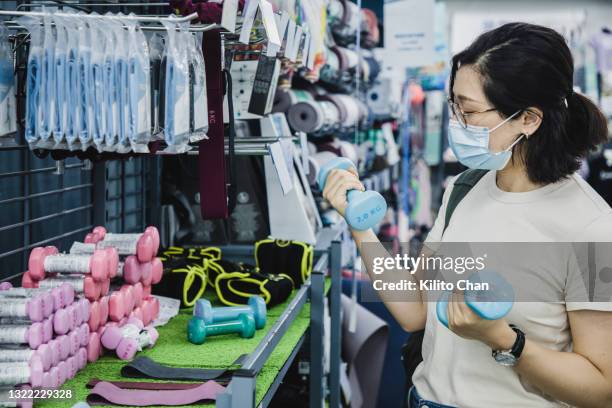 asian woman shopping for dumbbell in a sports shop - sports equipment store stock pictures, royalty-free photos & images