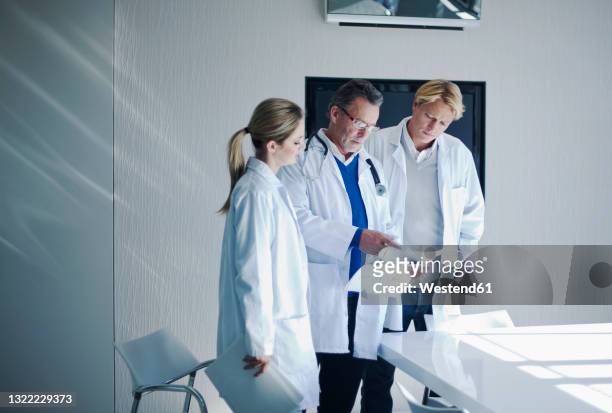 senior male doctor assessing paperwork to colleagues in hospital - medical judge stockfoto's en -beelden