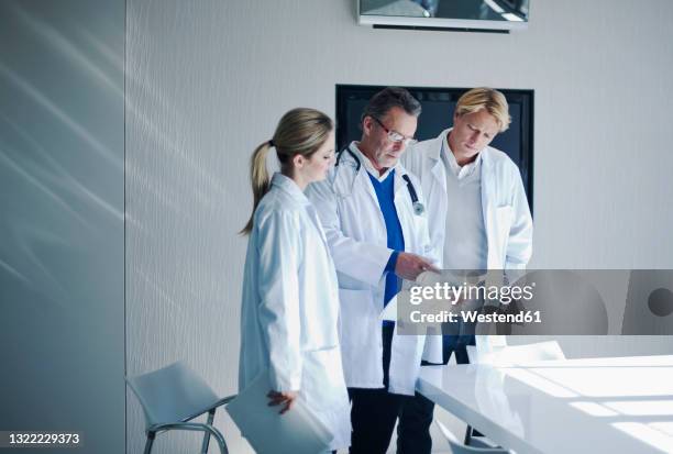 senior male doctor assessing paperwork to colleagues in hospital - judges table stock pictures, royalty-free photos & images