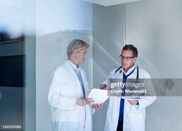 senior male doctor discussing over reports with young healthcare worker in hospital - talentrichter stock-fotos und bilder