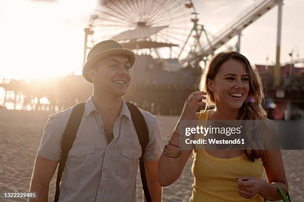 smiling couple looking away while enjoying vacations at santa monica pier - santa monica pier foto e immagini stock