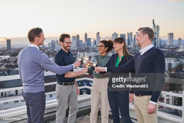 male and female colleagues toasting drinks after work on terrace - feierabend stock-fotos und bilder
