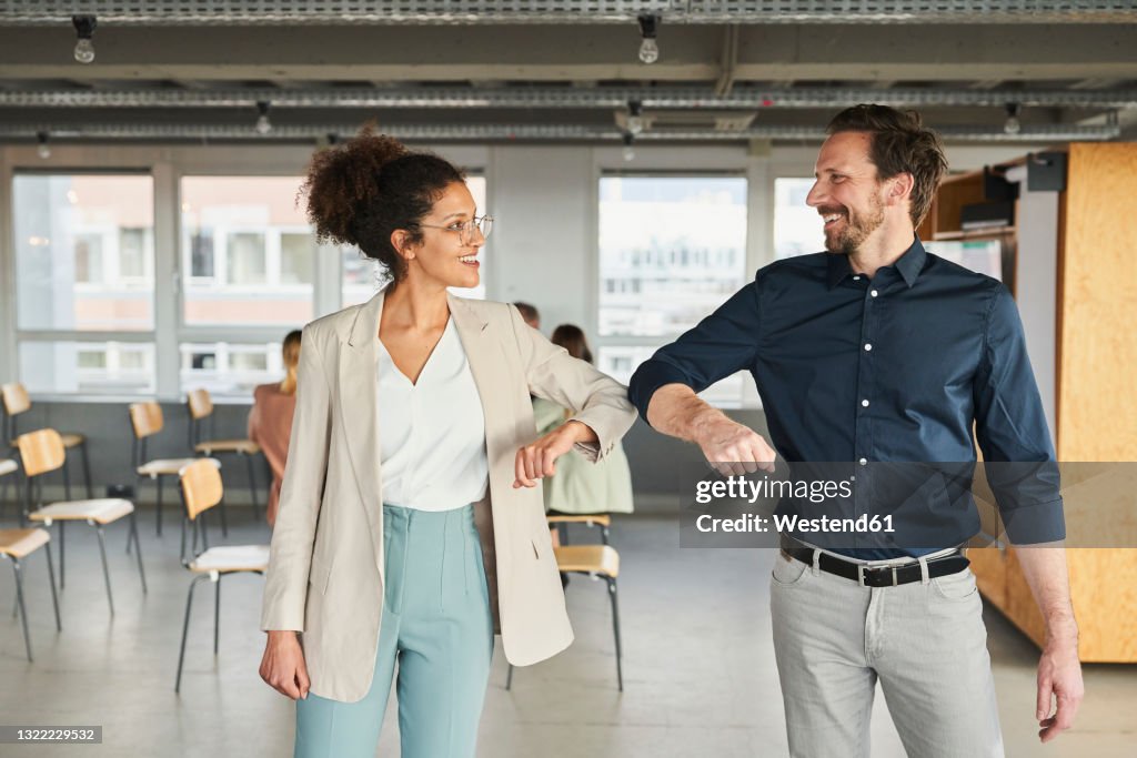 Male and female entrepreneurs smiling while greeting with elbow bumps in board room