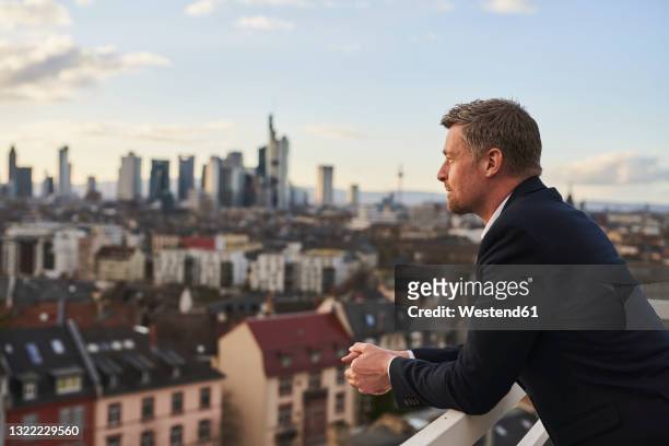 thoughtful mature businessman standing at rooftop in city - in die ferne schauen stock-fotos und bilder