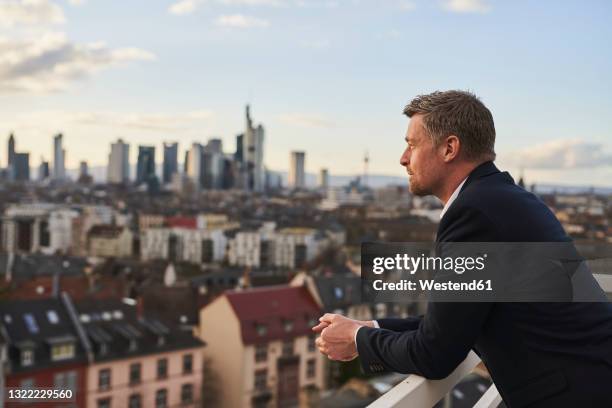 thoughtful mature businessman standing at rooftop in city - frankfurt germany skyline stock pictures, royalty-free photos & images