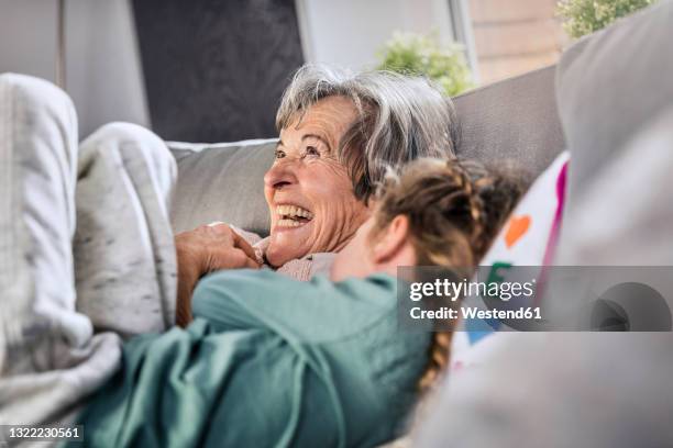 cheerful grandmother lying by granddaughter on sofa at home - granny stockfoto's en -beelden