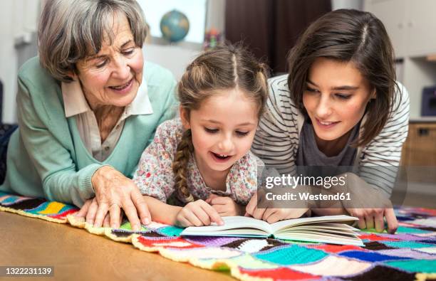 girl reading book while lying by women in nursery - mutter grossmutter kind stock-fotos und bilder