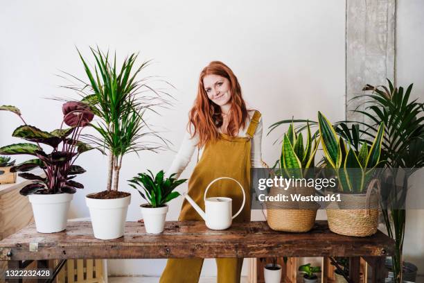 young woman standing in front of watering can at home - sansevieria stock pictures, royalty-free photos & images
