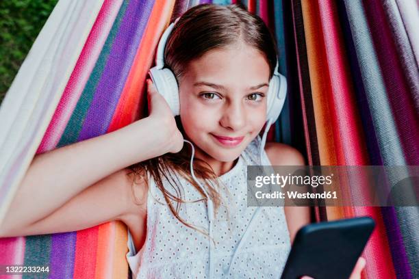 brown eyed girl listening music while relaxing in multi colored hammock - 子供のみ ストックフォトと画像