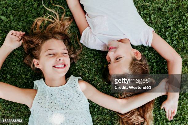 happy girls lying on grass in summer - side by side imagens e fotografias de stock