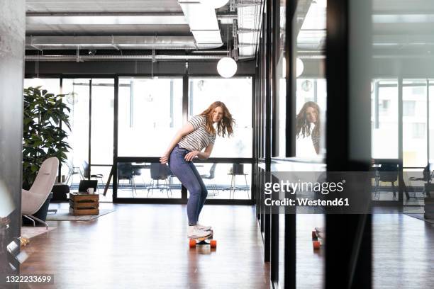 smiling female professional doing skateboarding in office - unusual imagens e fotografias de stock