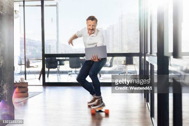 mature businessman skateboarding looking at laptop in office - action laptop stock pictures, royalty-free photos & images