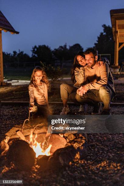 gelukkige familie die door het vreugdevuur in de achtertuin bij nacht geniet. - haardvuur stockfoto's en -beelden