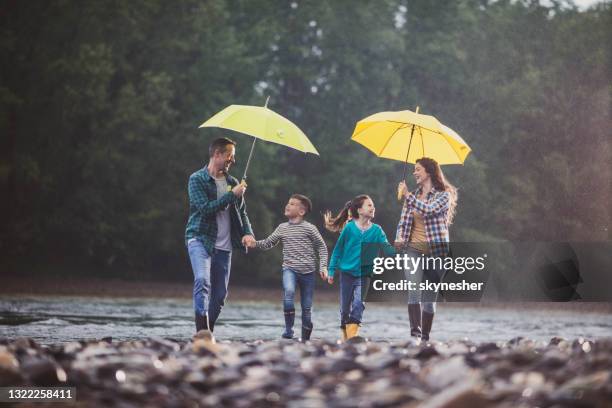 glückliche familie mit spaß beim laufen an einem regnerischen tag am flussufer. - mother protecting from rain stock-fotos und bilder